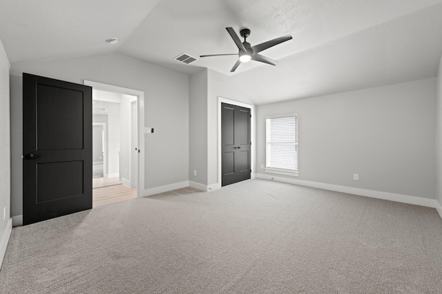 unfurnished bedroom with light carpet, a closet, vaulted ceiling, and ceiling fan