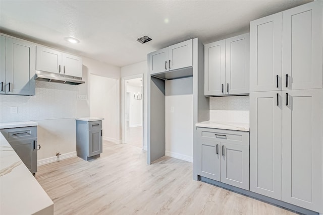 kitchen featuring gray cabinetry, light stone countertops, light wood-type flooring, and tasteful backsplash