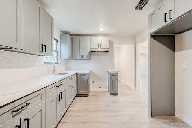 kitchen with gray cabinetry, backsplash, sink, and light hardwood / wood-style flooring