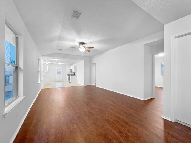 unfurnished living room with a wealth of natural light, ceiling fan, dark wood-type flooring, vaulted ceiling, and a textured ceiling