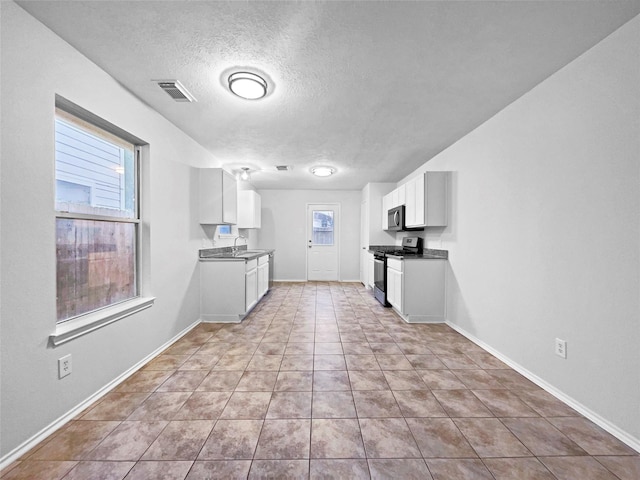 kitchen featuring sink, light tile patterned flooring, stainless steel range oven, a textured ceiling, and white cabinets