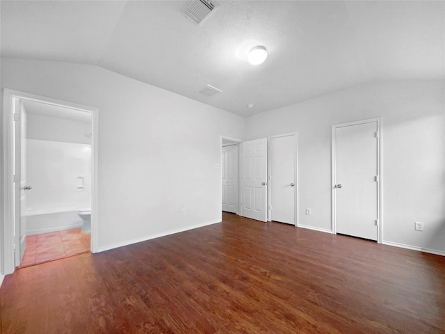 unfurnished bedroom with two closets, ensuite bathroom, dark hardwood / wood-style floors, and lofted ceiling