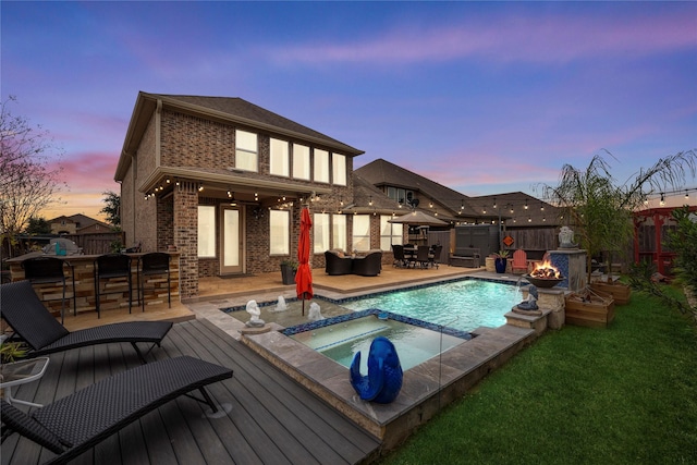 pool at dusk with an in ground hot tub, a bar, and an outdoor fire pit