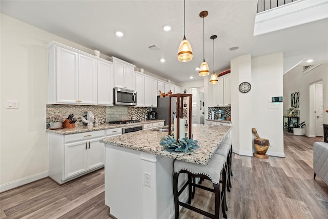 kitchen featuring light stone countertops, appliances with stainless steel finishes, white cabinetry, hanging light fixtures, and an island with sink