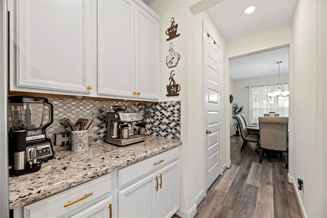 interior space with an inviting chandelier, white cabinets, hanging light fixtures, light hardwood / wood-style flooring, and tasteful backsplash