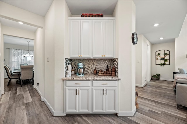 bar with white cabinets, light hardwood / wood-style floors, light stone countertops, and backsplash