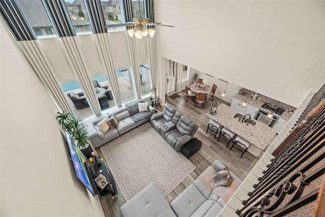 living room with hardwood / wood-style flooring, ceiling fan, and a towering ceiling