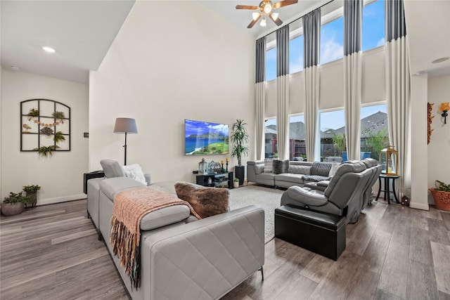 living room featuring ceiling fan, light hardwood / wood-style floors, and a high ceiling