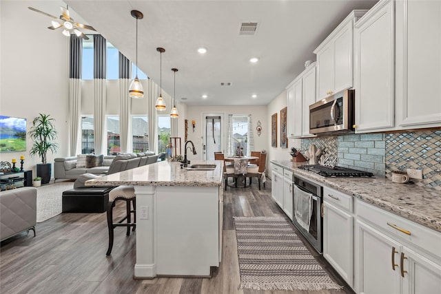 kitchen featuring stainless steel appliances, sink, decorative light fixtures, white cabinets, and an island with sink