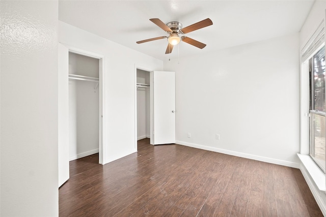 unfurnished bedroom featuring ceiling fan, dark wood-type flooring, and two closets