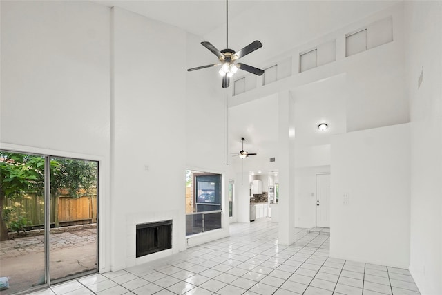 unfurnished living room with light tile patterned floors, a towering ceiling, ceiling fan, and a tiled fireplace