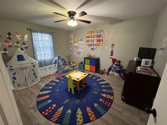 rec room with ceiling fan, hardwood / wood-style floors, and a textured ceiling