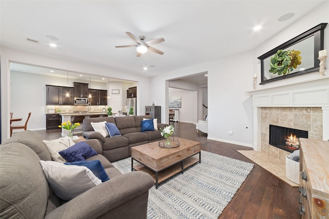 living room with dark wood-type flooring, ceiling fan, a tiled fireplace, and sink