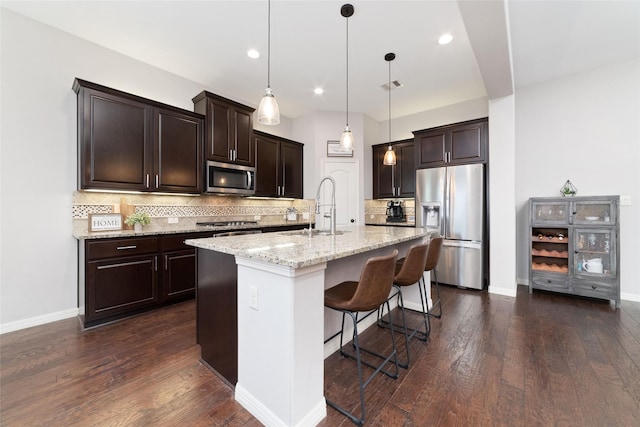 kitchen featuring sink, a kitchen breakfast bar, pendant lighting, stainless steel appliances, and a kitchen island with sink