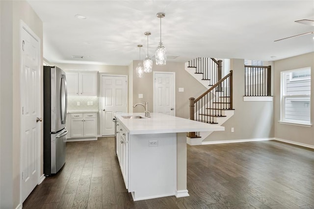 kitchen featuring decorative light fixtures, stainless steel fridge, a kitchen island with sink, backsplash, and white cabinetry