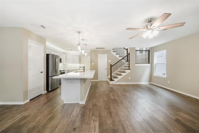 kitchen with a kitchen island with sink, stainless steel refrigerator, pendant lighting, sink, and white cabinetry