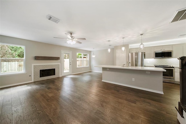 kitchen featuring decorative light fixtures, ceiling fan, backsplash, a kitchen island with sink, and appliances with stainless steel finishes