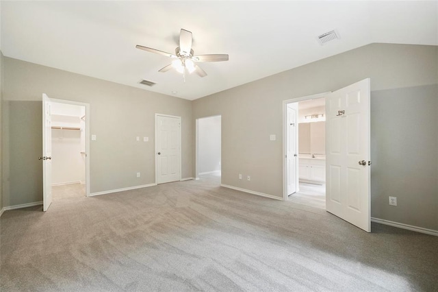 unfurnished bedroom featuring vaulted ceiling, a closet, light colored carpet, a walk in closet, and ceiling fan