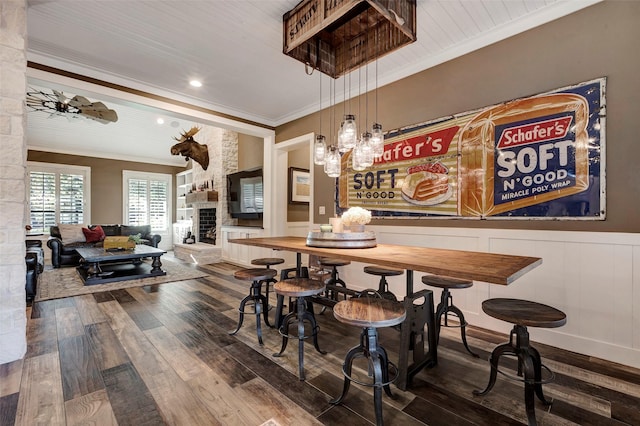 dining area with crown molding, a stone fireplace, and dark hardwood / wood-style floors