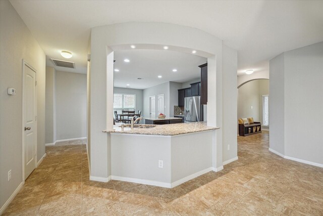 kitchen with kitchen peninsula, stainless steel fridge, light stone counters, and sink