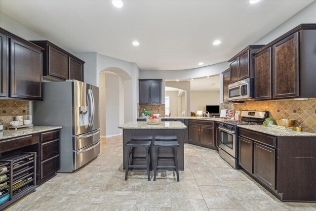 kitchen with a breakfast bar area, light stone counters, a center island, and stainless steel appliances