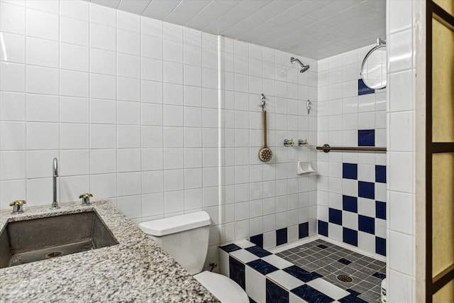 bathroom featuring tiled shower, toilet, tile walls, and sink