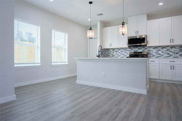 kitchen with white cabinets, stove, hanging light fixtures, and a kitchen island with sink