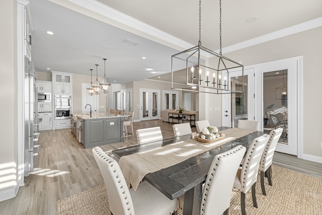 dining space with sink, ornamental molding, a chandelier, and light wood-type flooring