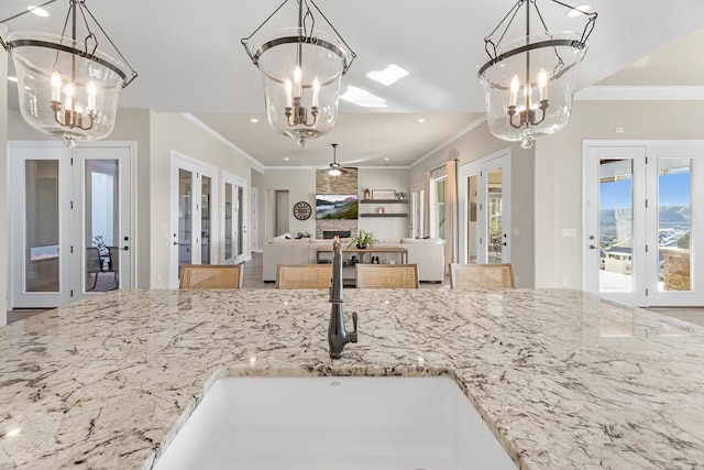 kitchen with french doors, ornamental molding, ceiling fan with notable chandelier, and light stone counters