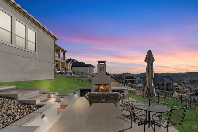 patio terrace at dusk featuring exterior fireplace and a yard