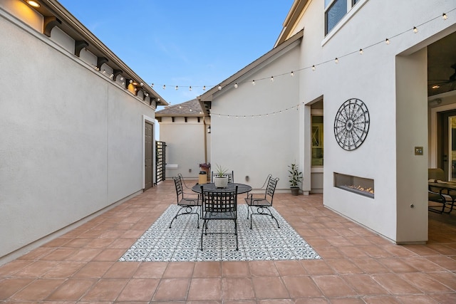 view of patio featuring outdoor dining space and a warm lit fireplace