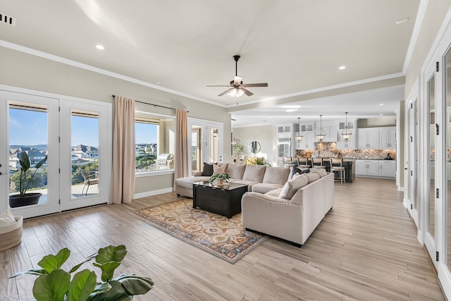 living area featuring visible vents, ornamental molding, light wood-type flooring, and a ceiling fan