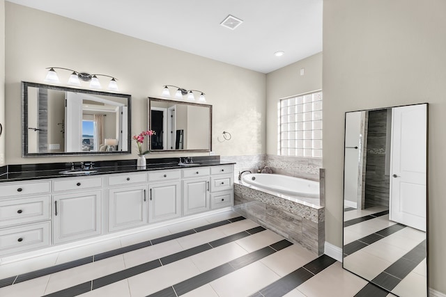 bathroom with tile patterned flooring, vanity, and a relaxing tiled tub