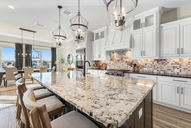 kitchen with white cabinetry, decorative light fixtures, and an island with sink