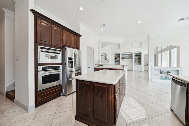 kitchen with appliances with stainless steel finishes, ornamental molding, built in shelves, dark brown cabinetry, and a center island