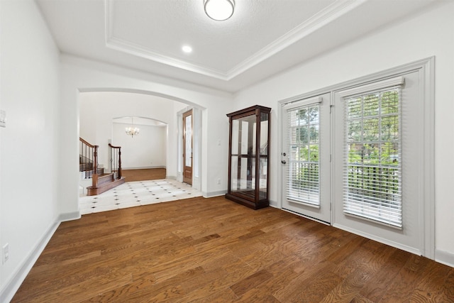 interior space with a raised ceiling, a chandelier, wood-type flooring, and ornamental molding