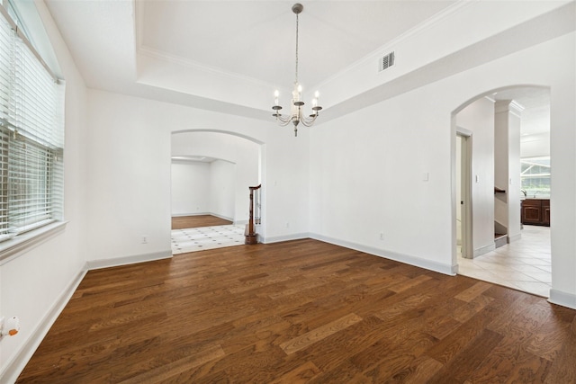 empty room featuring hardwood / wood-style floors, an inviting chandelier, a raised ceiling, and ornamental molding