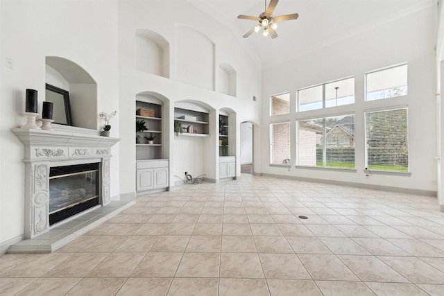 unfurnished living room featuring built in shelves, ceiling fan, a towering ceiling, and light tile patterned floors