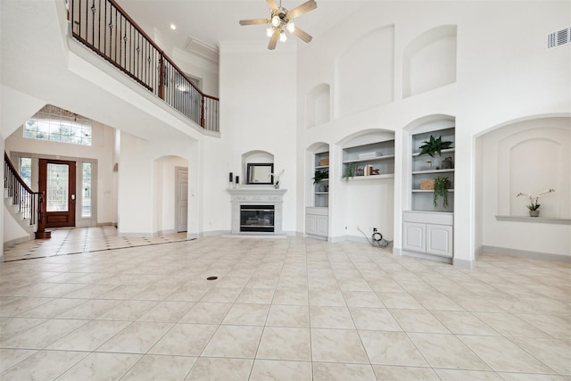 unfurnished living room with a towering ceiling, built in features, ceiling fan, and light tile patterned flooring