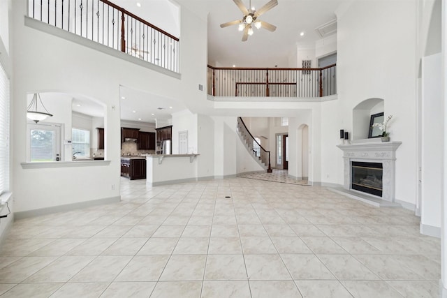 unfurnished living room with ceiling fan, light tile patterned floors, and a high ceiling