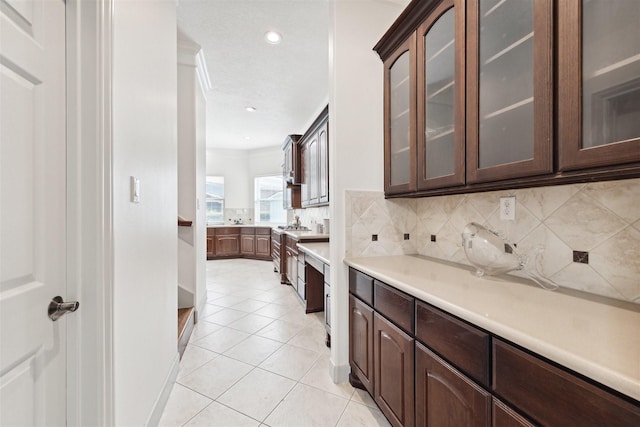 kitchen featuring decorative backsplash, dark brown cabinetry, crown molding, and light tile patterned flooring