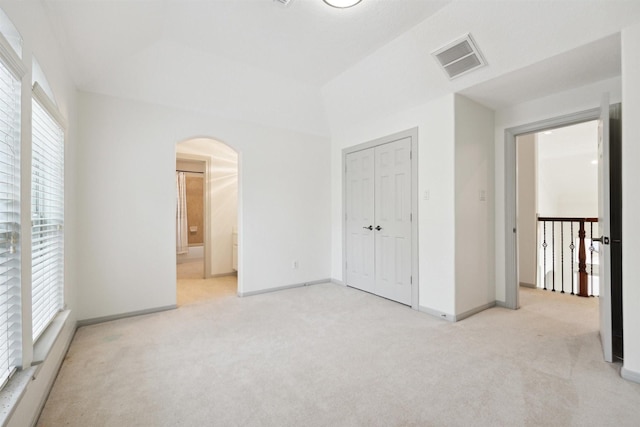 unfurnished bedroom featuring multiple windows, ensuite bathroom, a closet, and light carpet