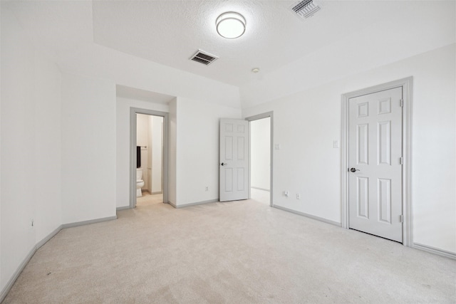 unfurnished bedroom featuring a textured ceiling, ensuite bathroom, and light carpet