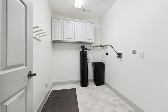 clothes washing area featuring cabinets, hookup for a washing machine, a textured ceiling, and light tile patterned flooring