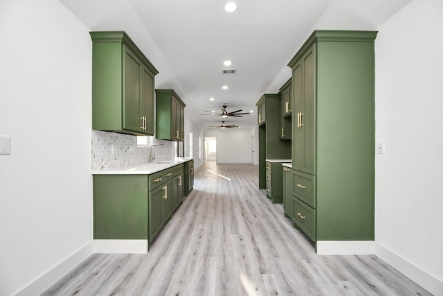 kitchen with ceiling fan, sink, green cabinets, backsplash, and light hardwood / wood-style floors