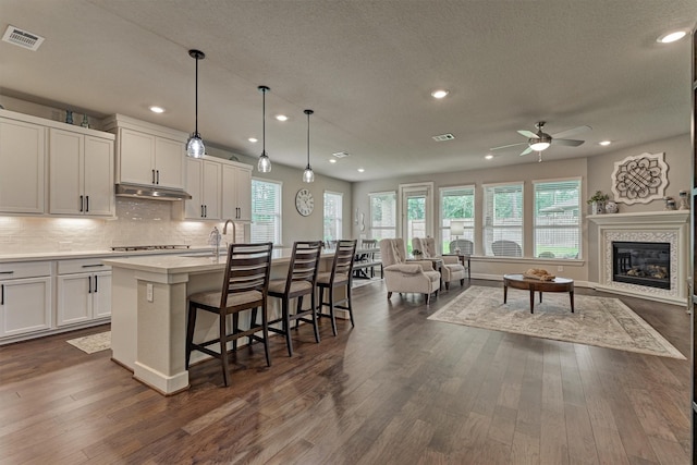 kitchen with a kitchen bar, a kitchen island with sink, decorative light fixtures, a premium fireplace, and white cabinetry