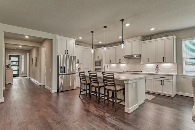 kitchen featuring decorative light fixtures, white cabinetry, stainless steel appliances, and a kitchen island with sink