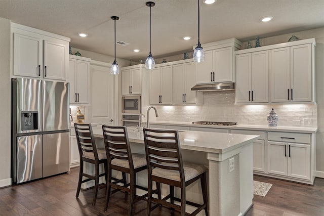 kitchen featuring white cabinets, dark hardwood / wood-style flooring, stainless steel appliances, and an island with sink