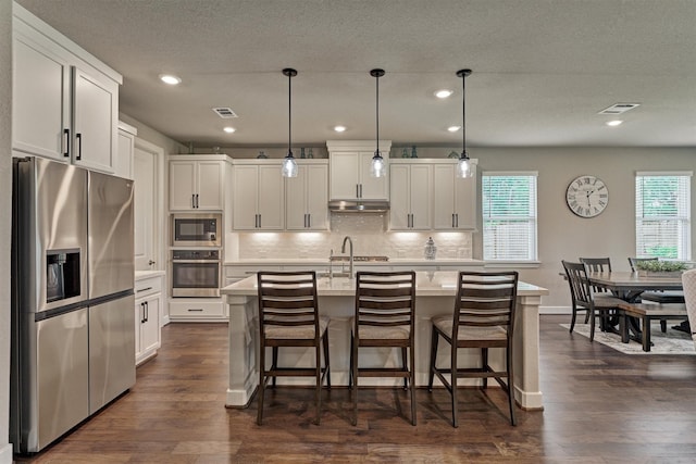 kitchen with appliances with stainless steel finishes, decorative light fixtures, white cabinetry, and an island with sink