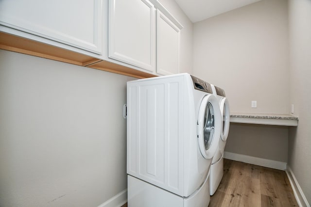 washroom with cabinets, washing machine and dryer, and light hardwood / wood-style floors